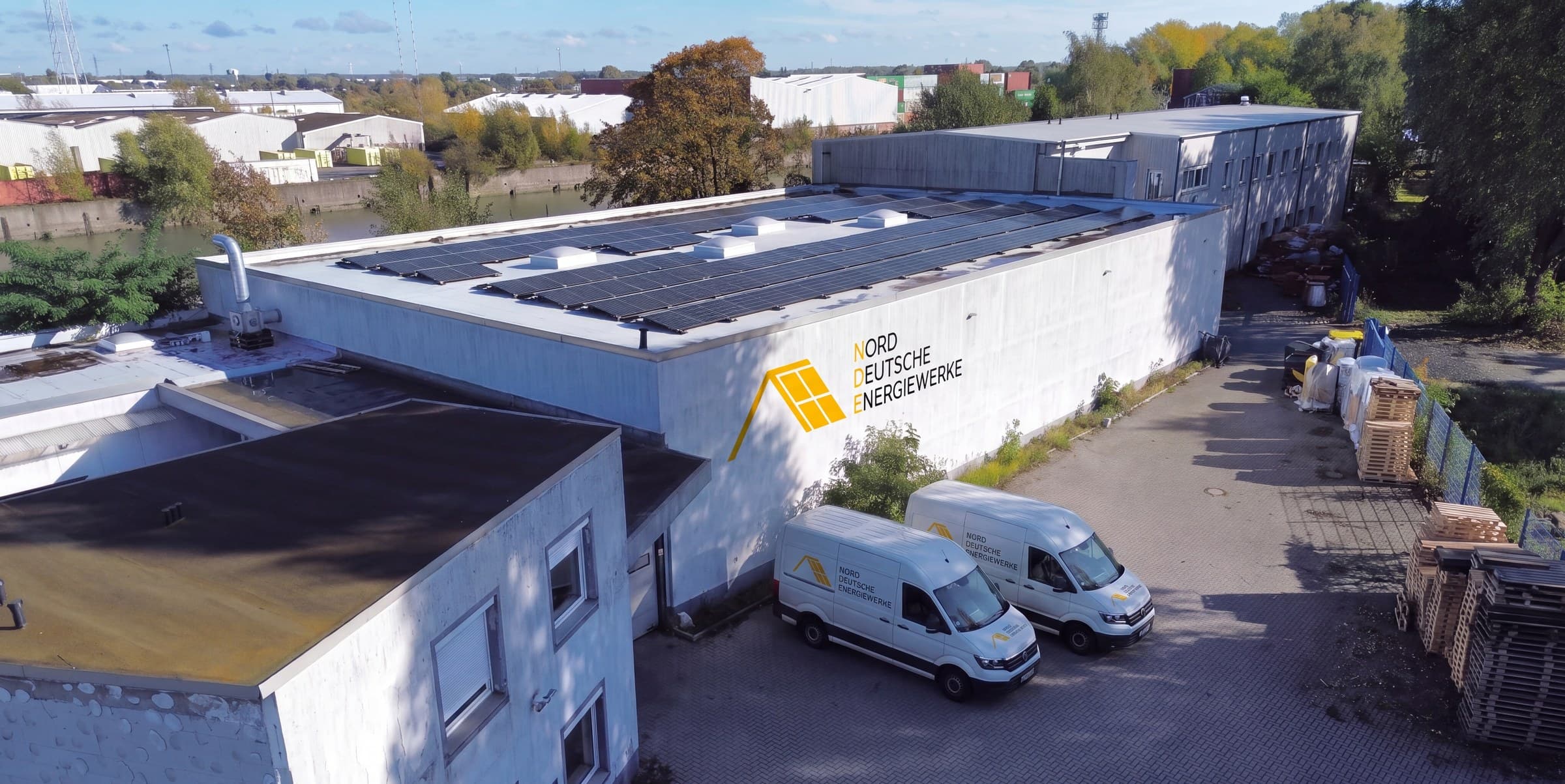 Unser Lager am Hamburger Hafen mit Solardach, Firmenschild und zwei Transportern